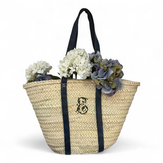Handwoven palm leaf basket with shoulder-length flat leather handles that are navy blue