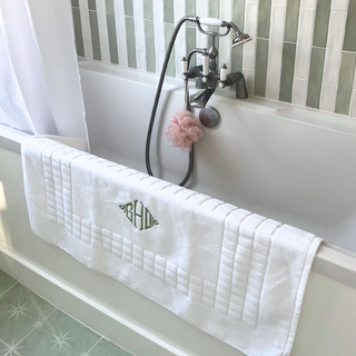 White quilted bath mat with monogram on a bathtub in a bathroom setting.