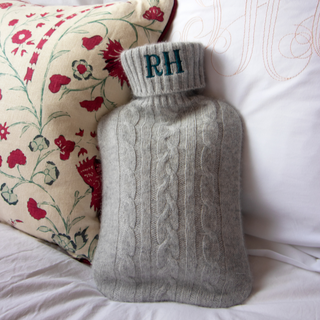 Gray knitted hot water bottle with 'RH' initials on a floral pillow embroidered by initially London