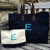 A Navy cotton canvas tote bag, with leather handles behind a navy and white pouch both with a large monogram