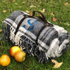 100% British wool with a nylon, water-resistant backing Picnic Rug in Grey Check in an outdoor setting. Monogrammed with a large single letter monogram  