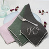 A large monogram on a brown napkin, which is on top of an olive and pink napkin. 