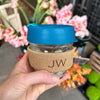 Glass keep cup, with a Multi-blue coloured lid, with a cork holder. The cork holder has a two letter etched monogram