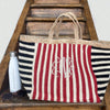 100% Organic Jute Striped Tote bag in white and Navy, with a large monogram at the front. placed on wooden steps with a monogrammed bottle by the side